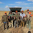 Photo of hunters with their birds near a truck in the field.